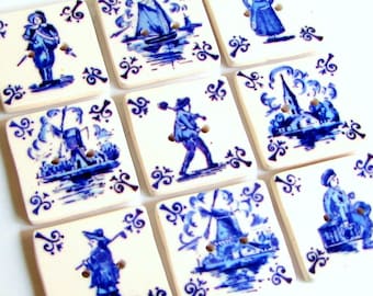 May include: Nine square ceramic buttons with blue and white Delft-style illustrations. Each button features a different scene of people, windmills, and boats. The buttons have two holes for sewing and decorative floral corner accents.