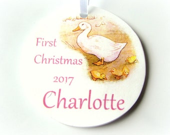 Op de afbeelding: Een ronde witte kerstbal met een afbeelding van een moeder eend en haar eendjes. De kerstbal is voorzien van de tekst "First Christmas 2017 Charlotte" in roze letters.