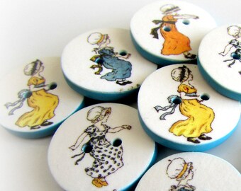 Op de afbeelding: Set van tien ronde, witte, houten knopen met een blauwe rand. Elke knop heeft een andere illustratie van een meisje dat een jurk draagt met een ander patroon en een andere kleur.