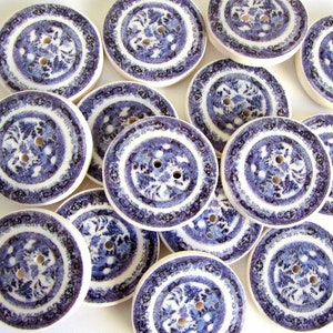 May include: A collection of 12 round, wooden buttons with a blue and white floral design. The buttons are approximately 2.5 cm in diameter.