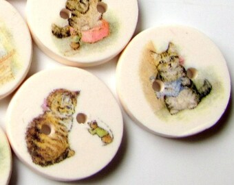 May include: Eight round wooden buttons with a white background and images of kittens in various poses. The kittens are depicted in a cartoon style with brown, white, and gray fur. Some kittens are holding objects like a ball of yarn or a mouse.