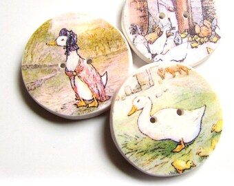 May include: Three round wooden buttons with images of ducks from the children's book, The Tale of the Two Bad Mice. The first button shows a duck wearing a hat, the second button shows a duck with ducklings, and the third button shows a woman standing in a doorway.