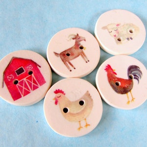 May include: Five round wooden buttons with different farm animal and barn designs. The buttons are white with red, brown, and black details. The designs include a red barn, a brown goat, a white sheep, a brown rooster, and a white hen.