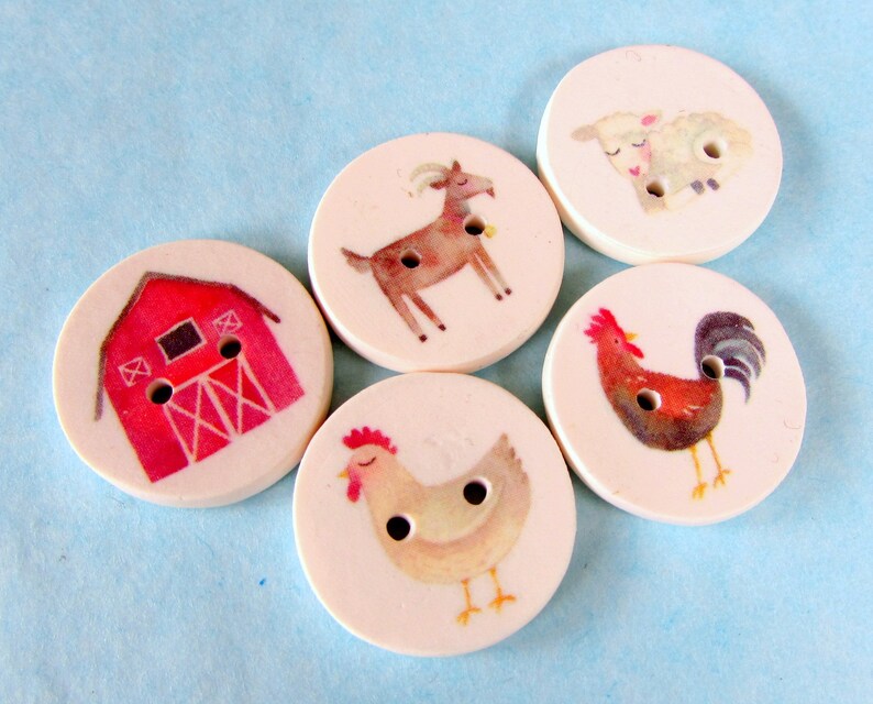 May include: Five round wooden buttons with different farm animal and barn designs. The buttons are white with red, brown, and black details. The designs include a red barn, a brown goat, a white sheep, a brown rooster, and a white hen.