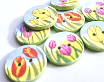 May include: A collection of round, flat buttons featuring printed illustrations of colorful tulips in shades of yellow, red, and pink against a light blue and green background. Each button has two small holes in the center for attachment purposes.