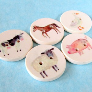 May include: Five round white ceramic buttons with different farm animal illustrations. The buttons feature a cow, a horse, a pig, a sheep, and a goose.