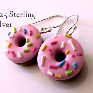 Könnte beinhalten: Ein Paar .925 Sterling Silber Donut-Ohrringe. Jeder rosa Donut ist mit bunten Streuseln verziert und hat eine braune Basis. Die Ohrringe haben silberne Haken.