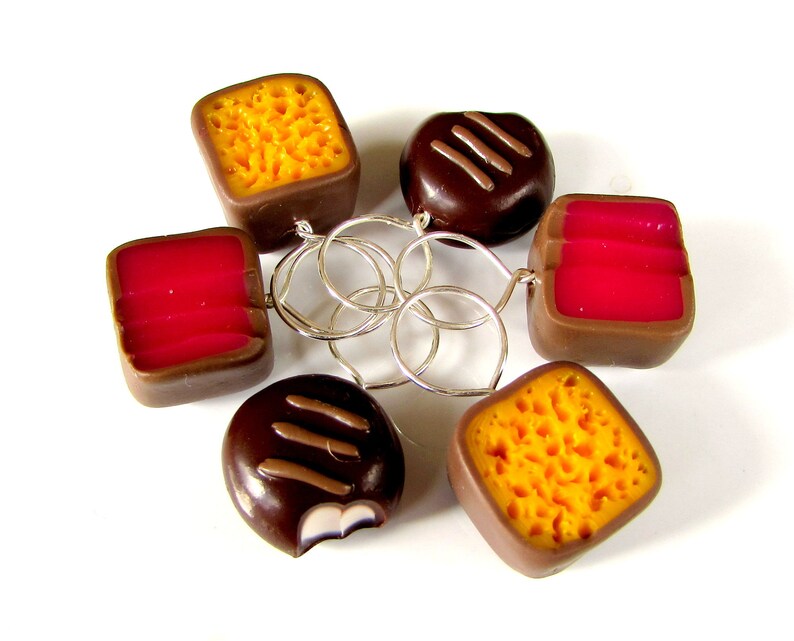 May include: A set of six chocolate and caramel candy charms with a honeycomb pattern, connected by silver rings. The charms are in the shape of squares and rectangles.