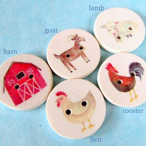May include: Set of 6 round wooden buttons with farm animal illustrations. The buttons feature a red barn, a white lamb, a brown goat, a brown rooster, a white hen, and a white goat. The buttons are approximately 1.5 inches in diameter.