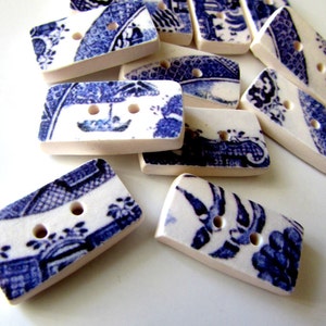 K&ouml;nnte beinhalten: Eine Ansammlung rechteckiger Kn&ouml;pfe mit blau-wei&szlig;em Blumenmuster. Die Kn&ouml;pfe haben zwei L&ouml;cher und einen cremefarbenen Rand. Diese Keramikkn&ouml;pfe eignen sich f&uuml;r verschiedene N&auml;hprojekte.