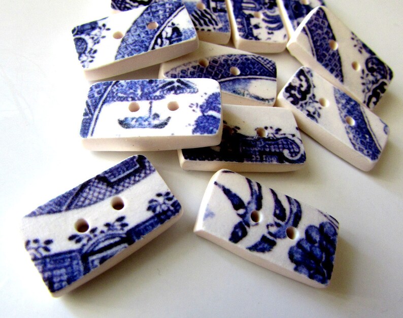 K&ouml;nnte beinhalten: Eine Ansammlung rechteckiger Kn&ouml;pfe mit blau-wei&szlig;em Blumenmuster. Die Kn&ouml;pfe haben zwei L&ouml;cher und einen cremefarbenen Rand. Diese Keramikkn&ouml;pfe eignen sich f&uuml;r verschiedene N&auml;hprojekte.