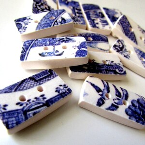 K&ouml;nnte beinhalten: Eine Sammlung rechteckiger Kn&ouml;pfe mit blau-wei&szlig;em Blumendesign. Jeder Knopf hat zwei L&ouml;cher und einen cremefarbenen Rand. Die Kn&ouml;pfe liegen auf einer wei&szlig;en Oberfl&auml;che.