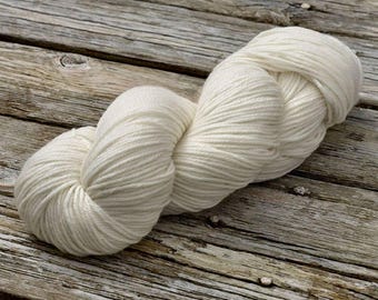 May include: A skein of white yarn, made of natural fibers, is shown on a rustic wooden surface.