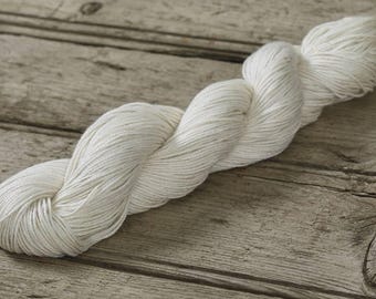 May include: A skein of white cotton yarn, twisted and coiled, on a rustic wooden surface.