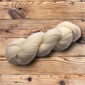 May include: A skein of off-white yarn, twisted into a loose braid, on a wooden surface.