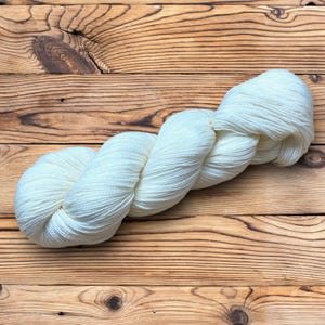Può includere: Un gomitolo di filato bianco su una superficie di legno.
