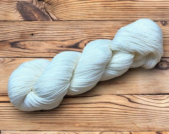 May include: A skein of white yarn on a wooden surface.