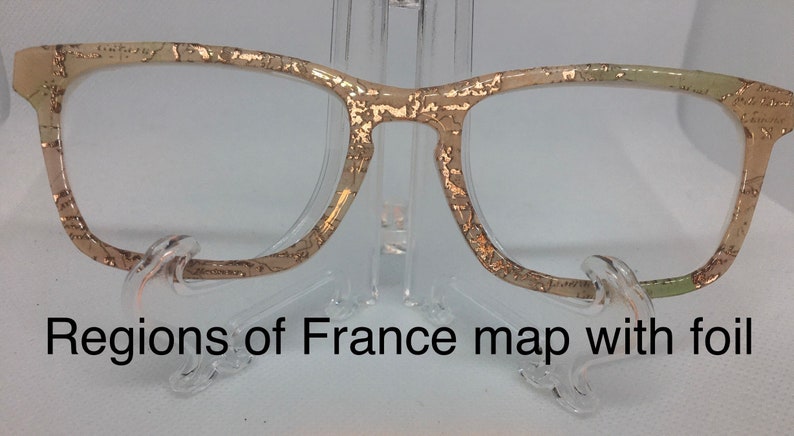 May include: Gold-toned glasses with a map of France printed on the frame. The map is in shades of beige and green with gold foil accents. "Regions of France map with foil" is printed below the glasses.
