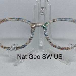May include: A pair of round, clear glasses with a white frame. The frame is printed with a map of the southwestern United States. The text "Nat Geo SW US" is printed below the glasses.