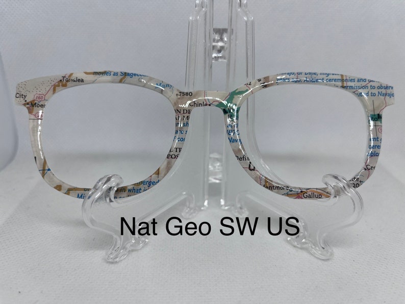 May include: A pair of round, clear glasses with a white frame. The frame is printed with a map of the southwestern United States. The text "Nat Geo SW US" is printed below the glasses.