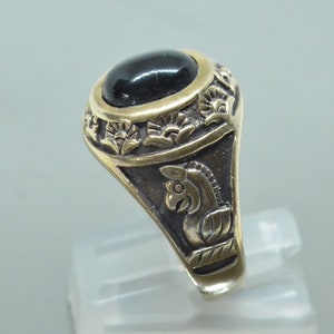 May include: A gold ring with a black gemstone and intricate floral designs. The ring features a detailed animal figure on the side.