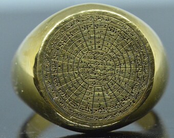 May include: A gold ring with a circular design featuring Arabic script and numbers. The ring is a signet style with a flat top and a rounded band.