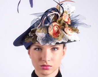 May include: A navy blue hat with a wide brim and a floral embellishment. The hat is decorated with pink, white, and green flowers, as well as a blue and white lace trim. The hat is accented with a long, dark blue feather.