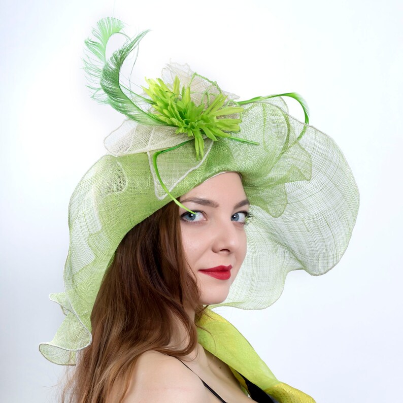 May include: A woman wearing a green and white hat with a flower and feather embellishment. The hat is made of a delicate, lacy material.