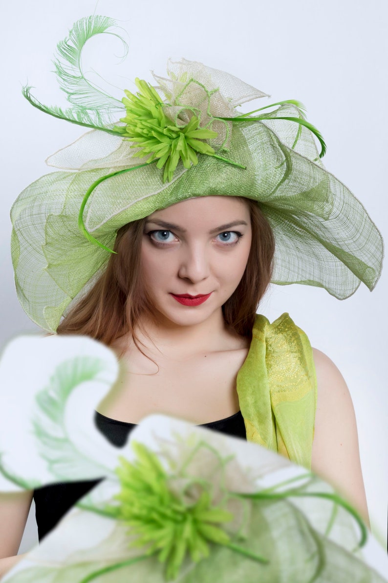 May include: A woman wearing a green and white hat with a green flower and a green scarf. The hat is made of a mesh material and has a wide brim.