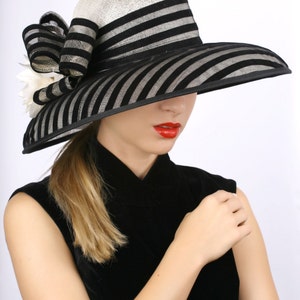 May include: A black and white striped hat with a wide brim and a white flower embellishment. The hat is made of straw and has a black ribbon around the crown.