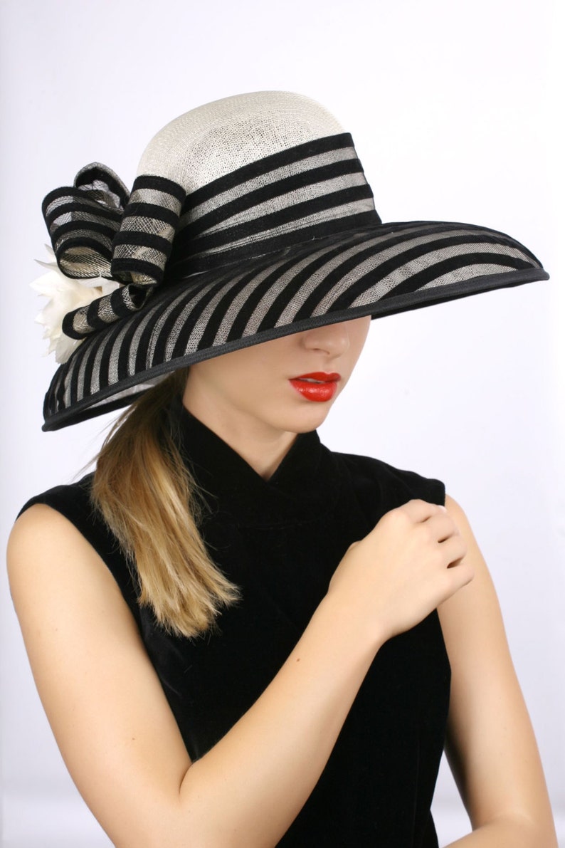 May include: A black and white striped hat with a wide brim and a white flower embellishment. The hat is made of straw and has a black ribbon around the crown.