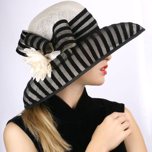 May include: A black and white striped hat with a large white flower accent. The hat is worn by a person with blonde hair and red lipstick. The person is wearing a black sleeveless dress.