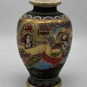 May include: A small, bulbous ceramic vase with a black base color, featuring intricate hand-painted figures in red, green, and blue robes. The design is accented with gold trim around the rim, neck, and base, and includes detailed gold patterns.