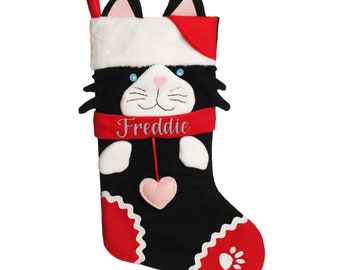 Può includere: Calza di Natale a forma di gatto nero e bianco con bordino rosso e bianco. La calza ha un polsino in pelliccia bianca, un cappello rosso e un cuore rosa. La calza è personalizzata con il nome "Freddie".