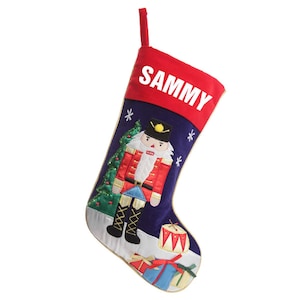 May include: A blue and red Christmas stocking with a nutcracker design. The stocking has a red cuff with the name "SAMMY" embroidered in white.