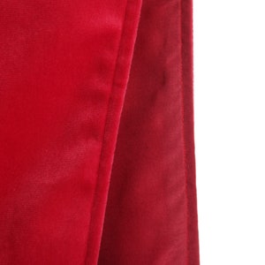 Puede incluir: Primer plano de una sección de tela de terciopelo rojo. La tela está doblada, revelando una costura y una textura contrastante. El color rojo intenso y profundo es consistente en toda la imagen, destacando el material lujoso.