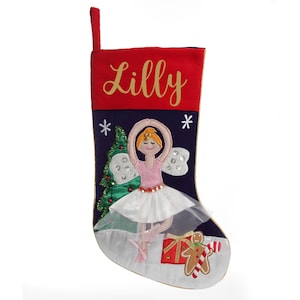 May include: A festive Christmas stocking with a red top and navy blue body. It features a ballerina, a Christmas tree, and a gingerbread man. The name "Lilly" is embroidered in gold.