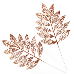 Può includere: Due steli di foglie decorative color bronzo con intricati disegni di foglie traforate. Le foglie hanno una finitura glitterata e gli steli sono sottili e simili a fili. Le foglie sono disposte simmetricamente su uno sfondo bianco.