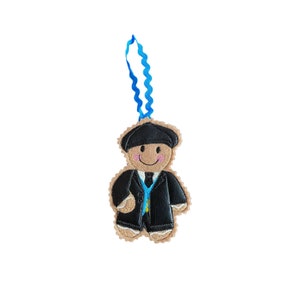 May include: A gingerbread person ornament with a black suit and blue tie. The ornament is hanging from a blue ribbon.