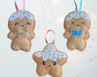 May include: Three felt Christmas ornaments: two gingerbread men and a star. The gingerbread men have white icing with colorful sprinkles and pink or blue ribbon hangers. The star has white icing with colorful sprinkles and a pink ribbon hanger. All have smiling faces.