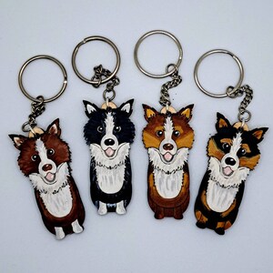 May include: Four wooden dog keychains with painted faces. The dogs are a black and white border collie, a brown and white border collie, a tri-color border collie, and a black and white Australian shepherd.