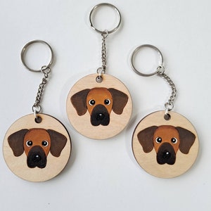 May include: Three wooden keychains with a brown and black dog illustration. Each keychain has a silver metal ring and chain.