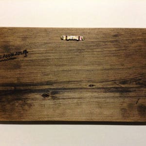 K&ouml;nnte beinhalten: R&uuml;ckseite eines rechteckigen Holzschildes mit nat&uuml;rlicher Holzmaserung. Oben ist ein S&auml;gezahnaufh&auml;nger aus Metall angebracht. Die Worte "Rustic Apple Art" sind auf der linken Seite aufgedruckt.