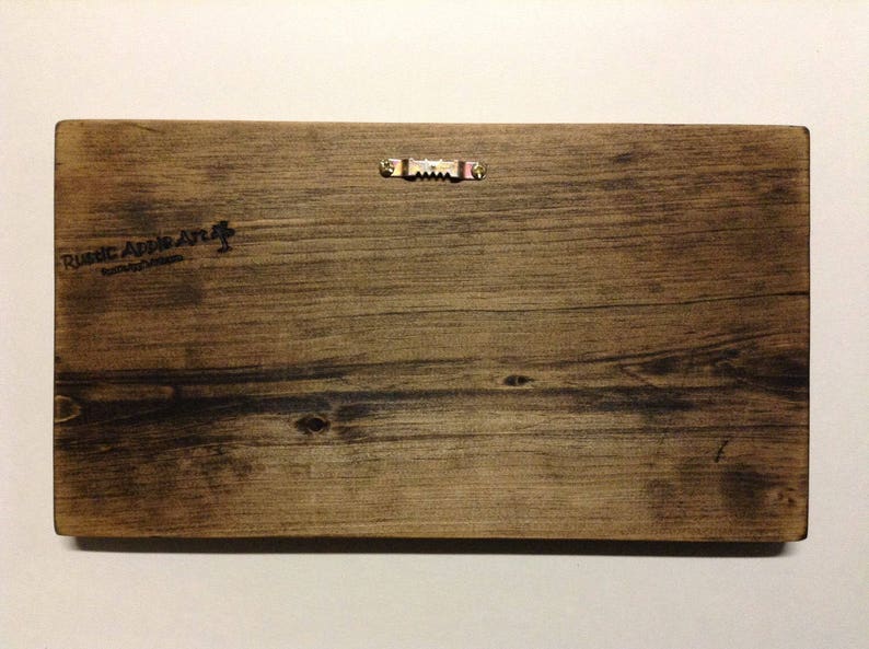 K&ouml;nnte beinhalten: R&uuml;ckseite eines rechteckigen Holzschildes mit nat&uuml;rlicher Holzmaserung. Oben ist ein S&auml;gezahnaufh&auml;nger aus Metall angebracht. Die Worte "Rustic Apple Art" sind auf der linken Seite aufgedruckt.