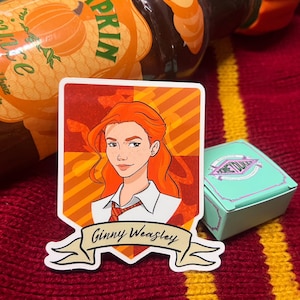 May include: A sticker featuring a cartoon illustration of Ginny Weasley with red hair, wearing a white shirt and red tie. The sticker has a banner that reads "Ginny Weasley". A teal box with the text "Honeydukes" is also visible.