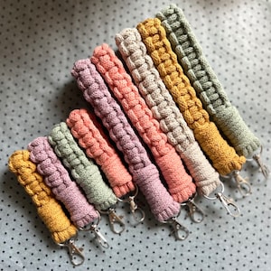 May include: A set of eight colorful crocheted keychains with silver key rings. The keychains are made with a variety of colors, including yellow, orange, pink, and green.
