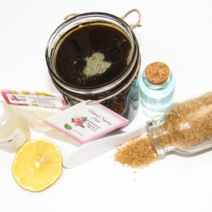 An 8 oz jar of Sugaring Paste is with included pouch of cornstarch, bottle of aloe vera & applicator next to a slice of lemon, a glass jar filled with clear water, and another jar tipped over, spilling raw sugar, accentuating the natural ingredients.