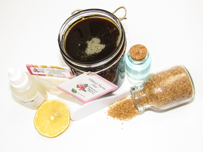 An 8 oz jar of Sugaring Paste is with included pouch of cornstarch, bottle of aloe vera & applicator next to a slice of lemon, a glass jar filled with clear water, and another jar tipped over, spilling raw sugar, accentuating the natural ingredients.