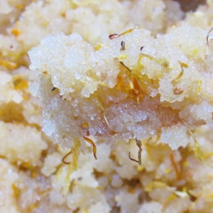 Close-up view of orange calendula sugar scrub in a bowl with a wooden spatula, highlighting its grainy texture and orange color.