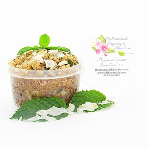 A 2 oz tub of cooling peppermint and coconut cane sugar scrub offers a refreshing and hydrating experience for your skin. The sugar scrub is centered, near bright green sprigs of peppermint and coconut flakes are scattered throughout the arrangement.